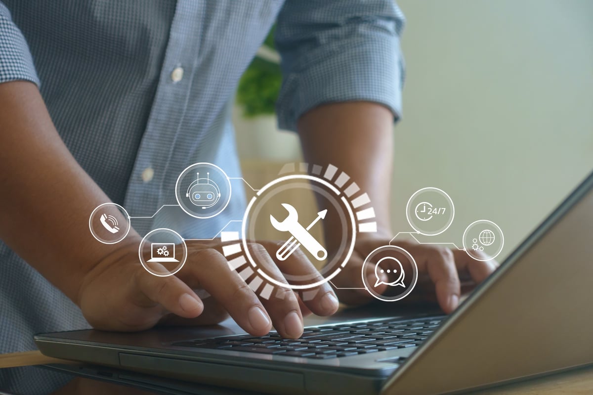 Man typing on laptop with digital interface icons showing tools, chatbot and 24/7 service